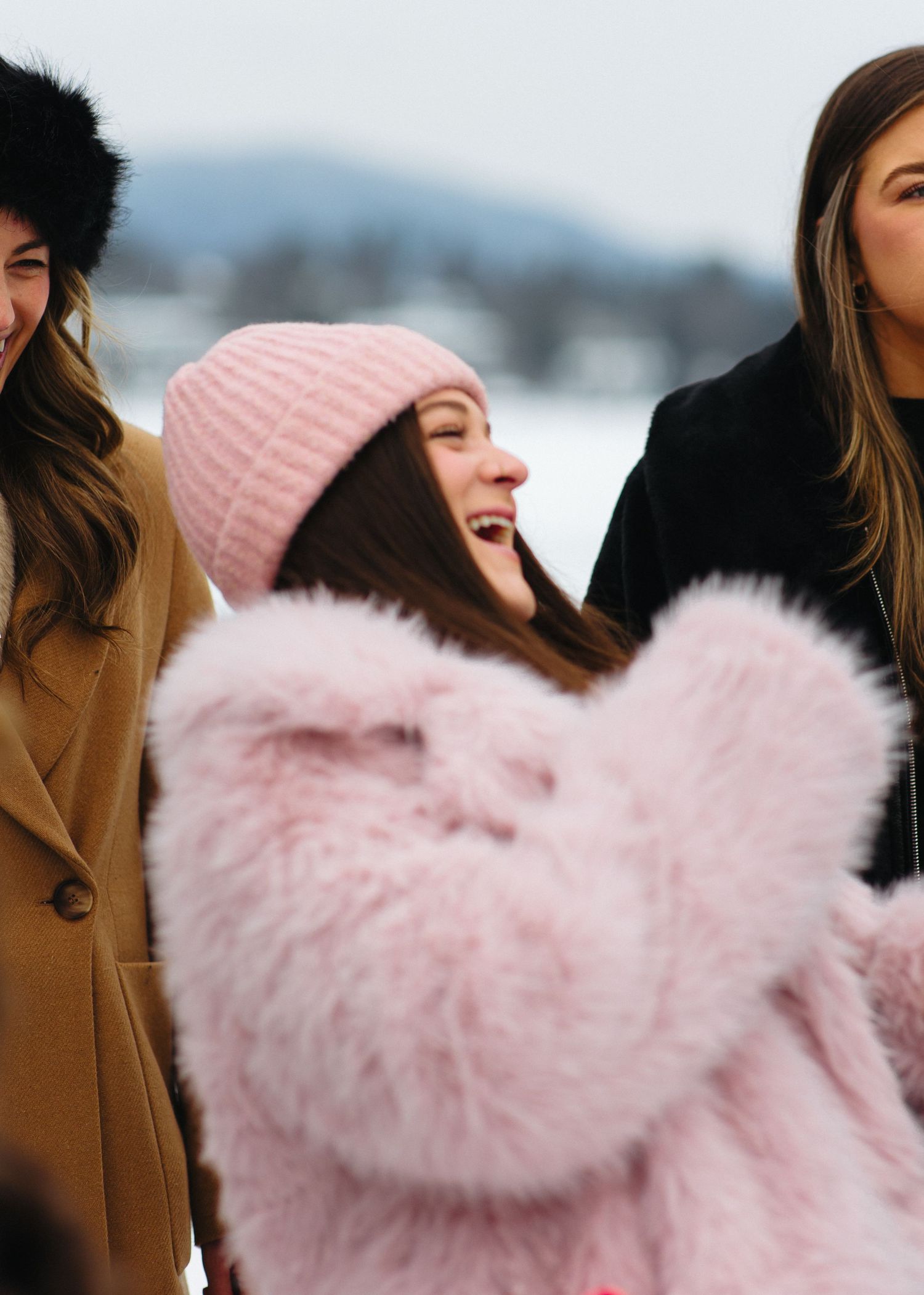 People wearing winter coats and pink fuzzy jackets in snowy setting.