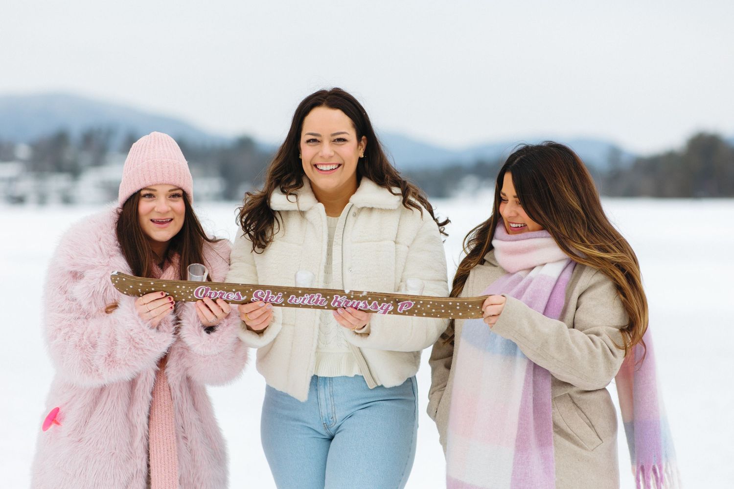 Friends linking arms while walking together in snow wearing winter coats.