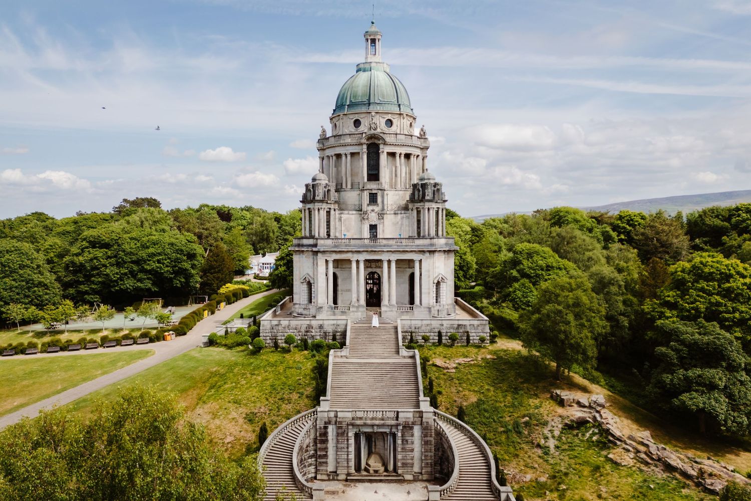 Scenic panoramic view of a historic domed church building nestled among green trees on a hilltop against cloudy skies.