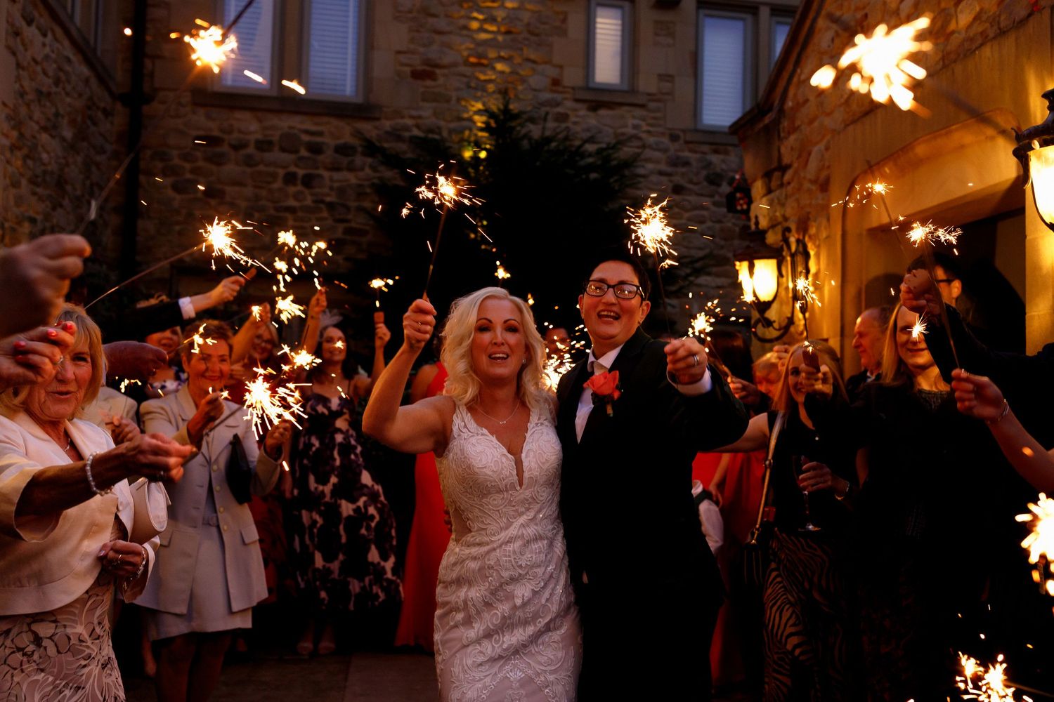 Wedding guests celebrate with sparklers during an evening celebration at a rustic stone venue.