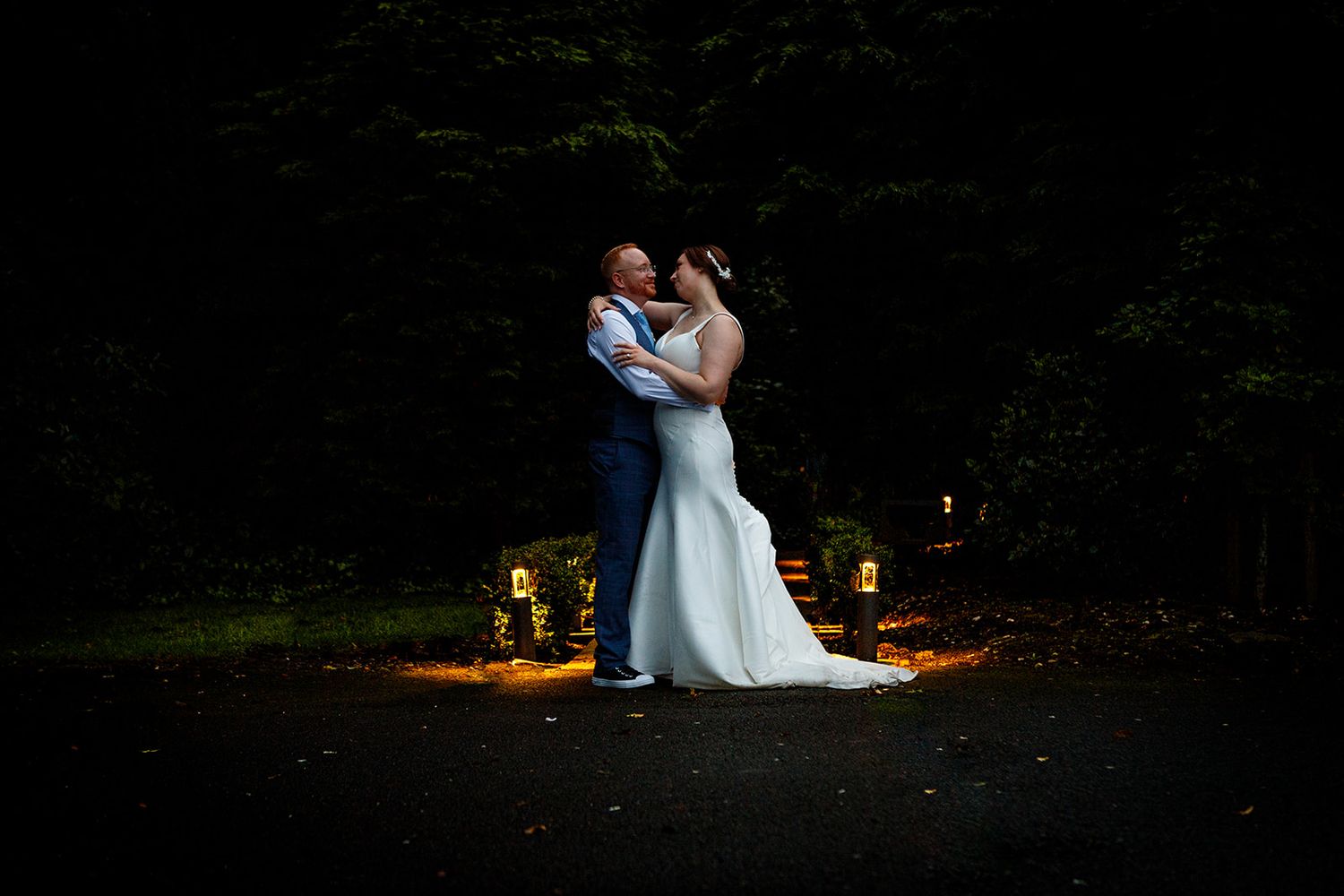 Romantic nighttime wedding portraits with couples silhouetted against warm outdoor lighting in a garden setting.