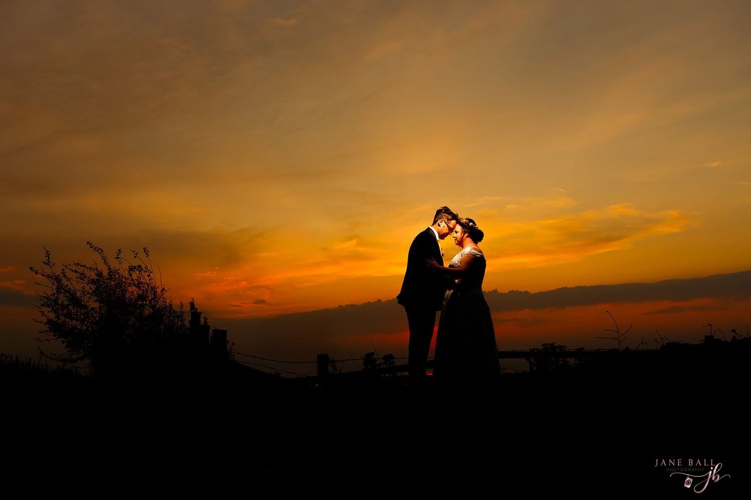 A silhouette of trees and mountains against a dramatic orange and golden sunset sky.