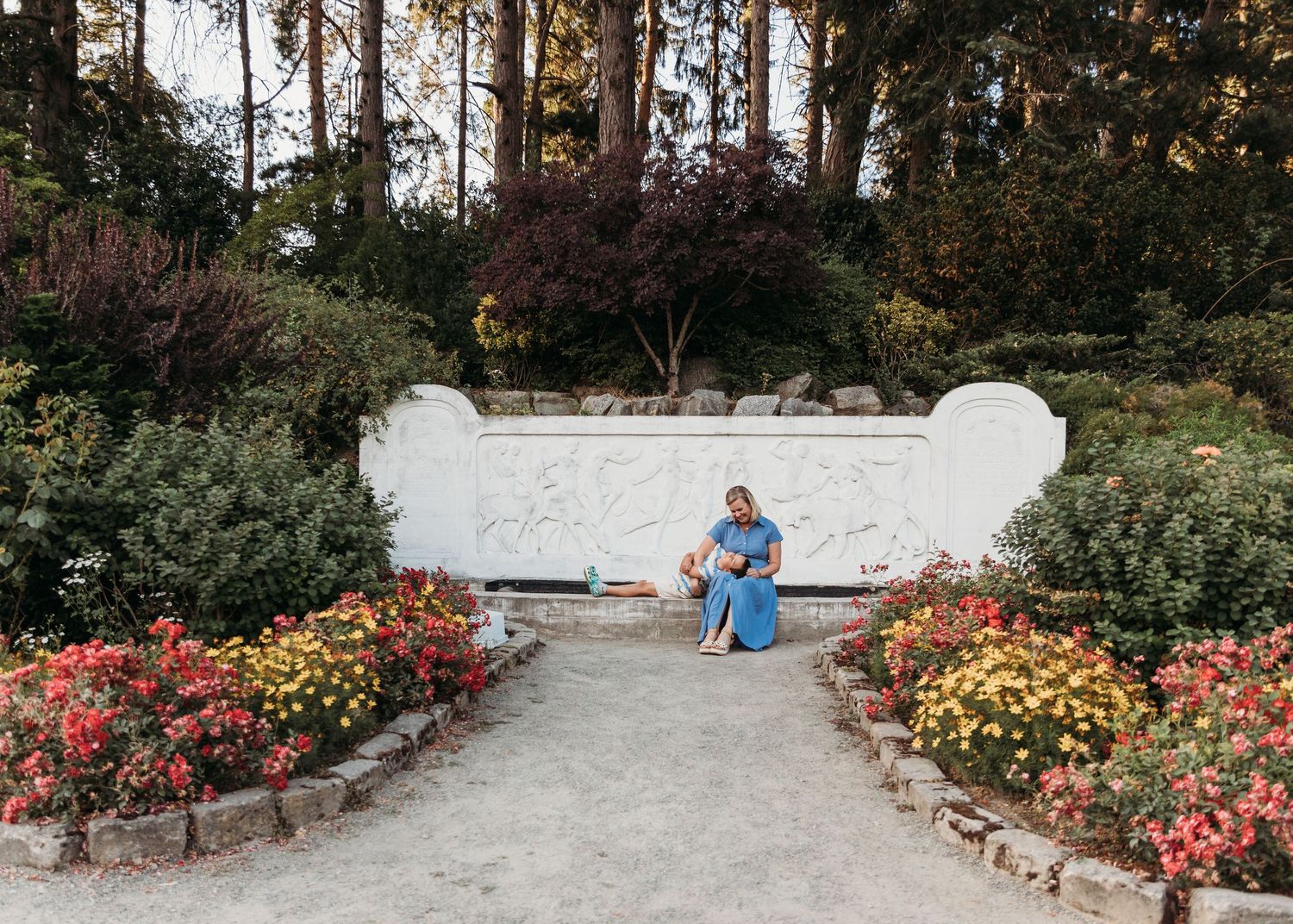 A panoramic view of a curved garden path lined with colorful roses and flowering plants in a park setting.