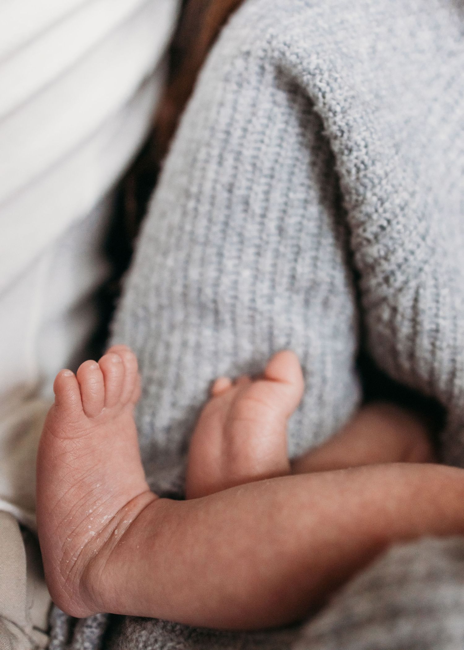 A close-up view of a baby's tiny hand reaching out from a soft gray knitted blanket.