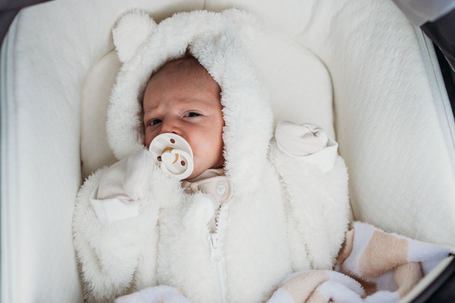 A sleeping baby wrapped in white blankets and bedding lies peacefully in a crib.