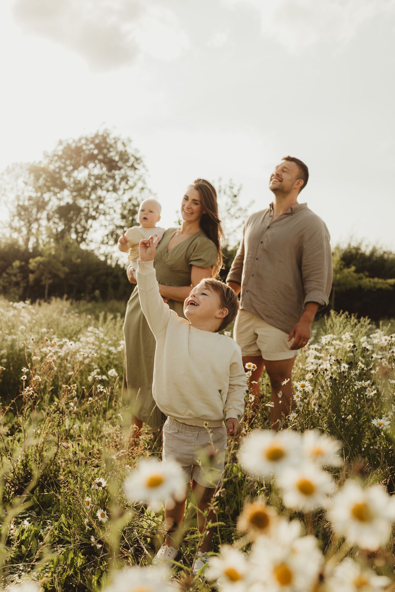 A child in a brown dress and white blouse plays outdoors in a grassy field at sunset.
