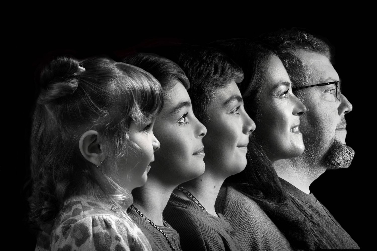 Black and white profile portraits of multiple generations looking upward against dark background.
