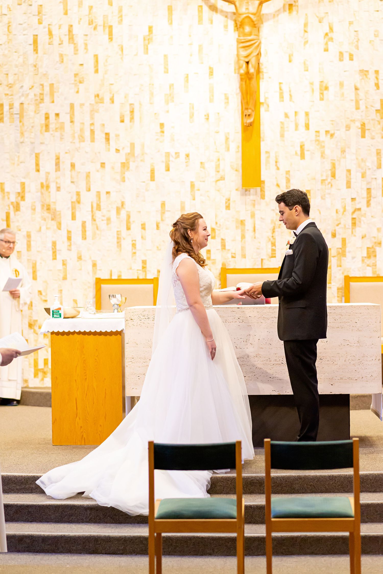 A couple stands at the altar during their wedding ceremony in a modern church with white and gold decor.