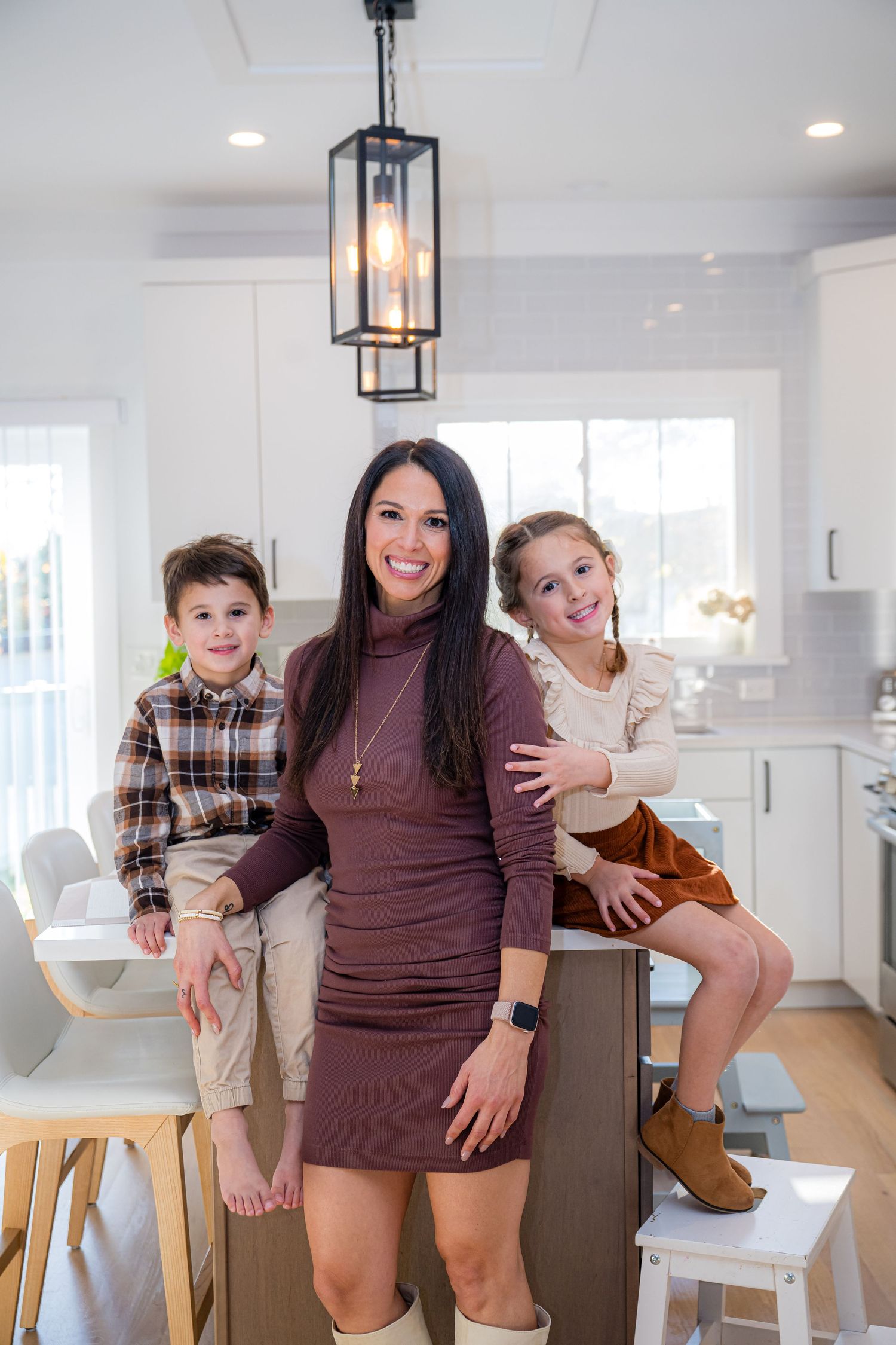A group poses together in a modern white kitchen with pendant lighting and hardwood floors.