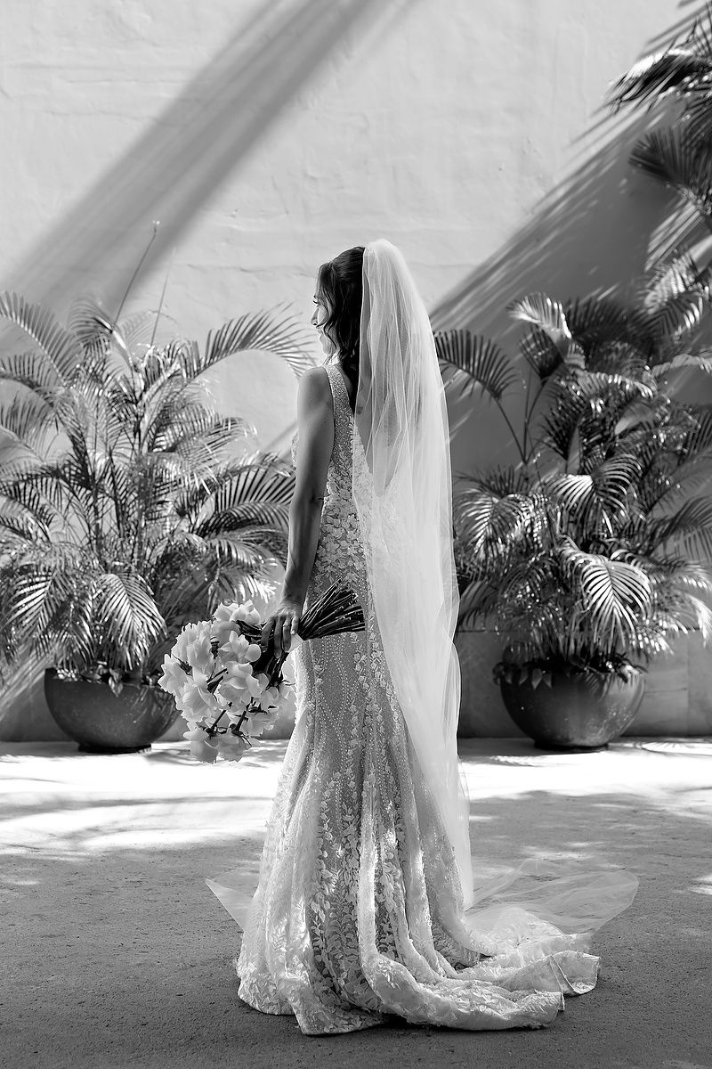 A series of black and white bridal portraits showing a flowing lace wedding dress against a backdrop of palm trees.