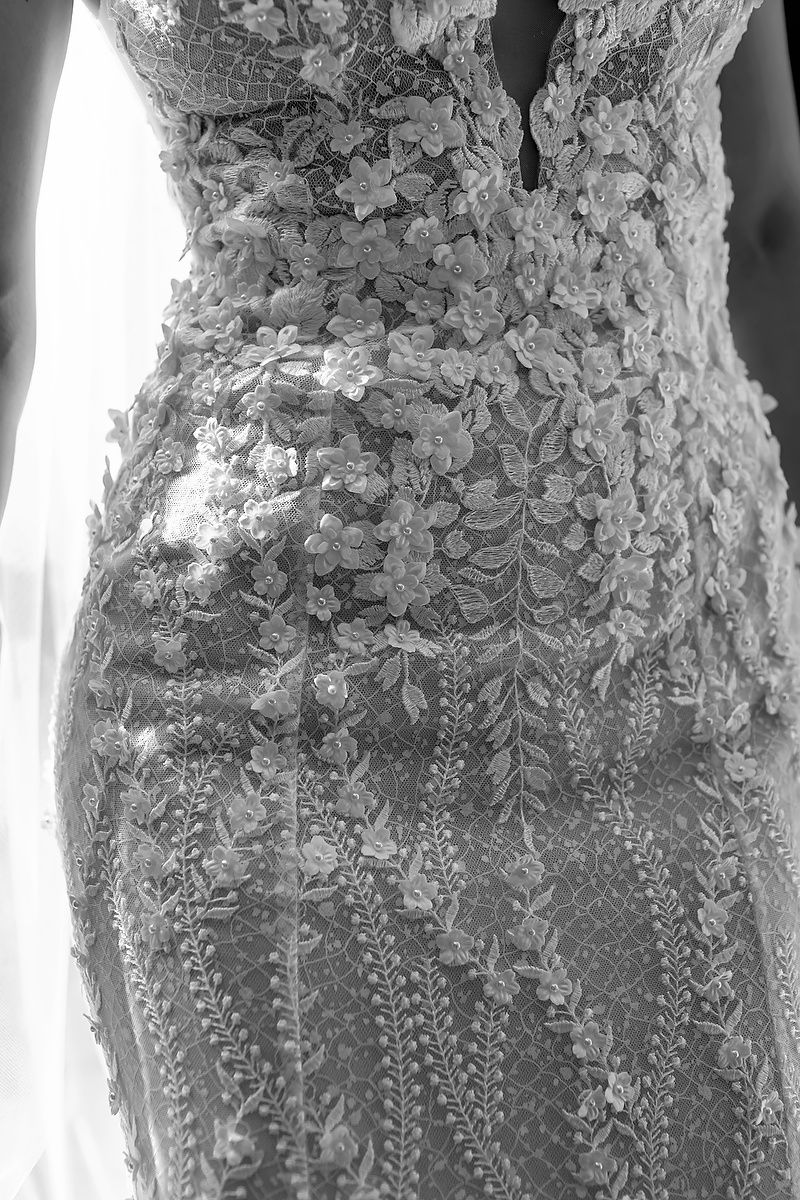 Elegant lace wedding dress with intricate floral patterns and cascading details shown in black and white photography.