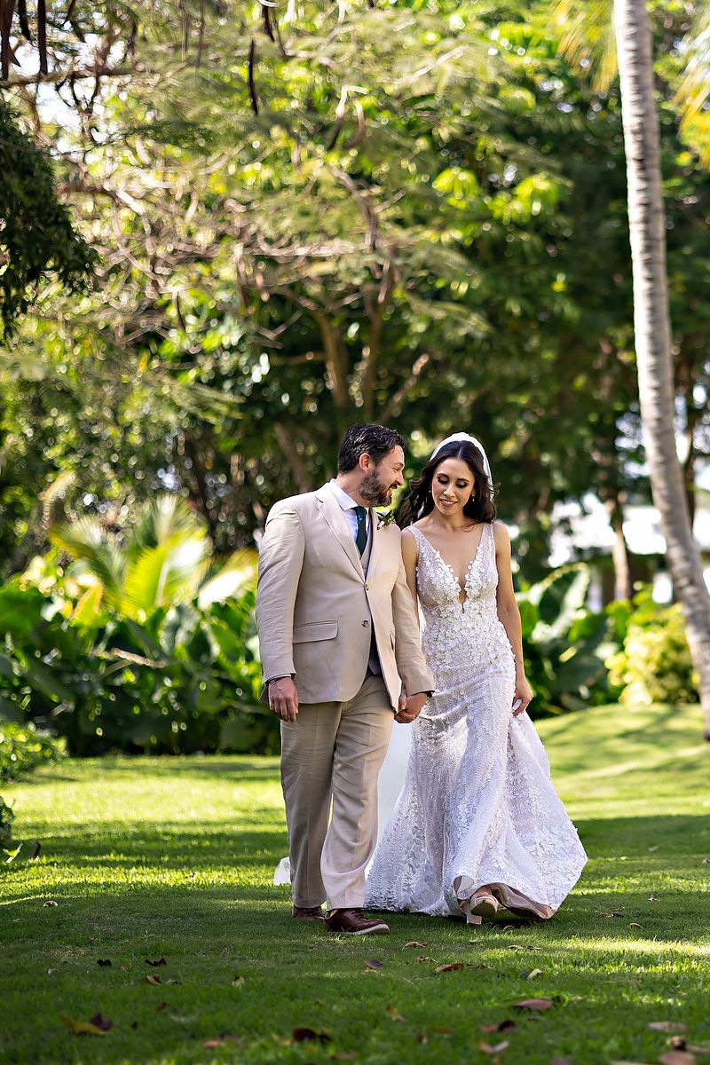 A couple walks together on a lush green lawn surrounded by tropical foliage during a garden wedding ceremony.