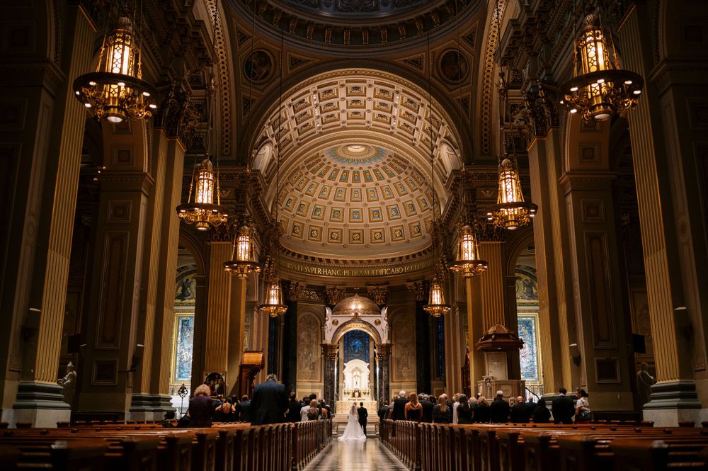 Ornate church interior with dramatic domed ceiling, hanging chandeliers and long center aisle.