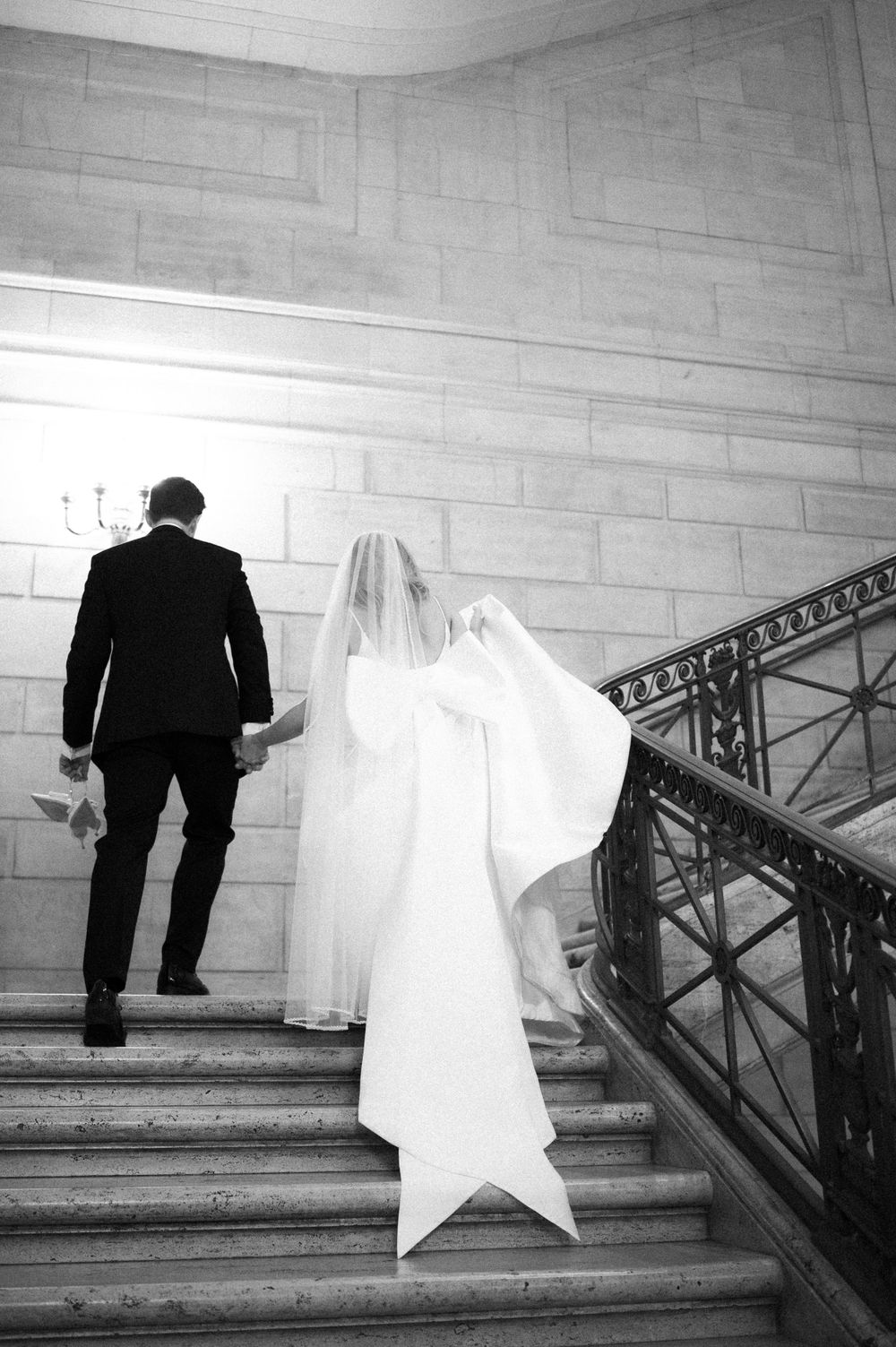 Black and white photo of couple ascending grand marble staircase.