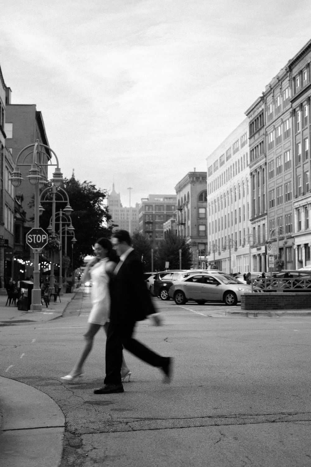 Black and white street scene showing motion blur of people walking past a stop sign on an urban corner.