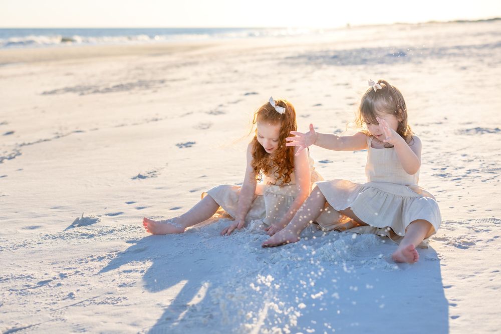 People playing and splashing in shallow ocean waves at sunset on a sandy beach.