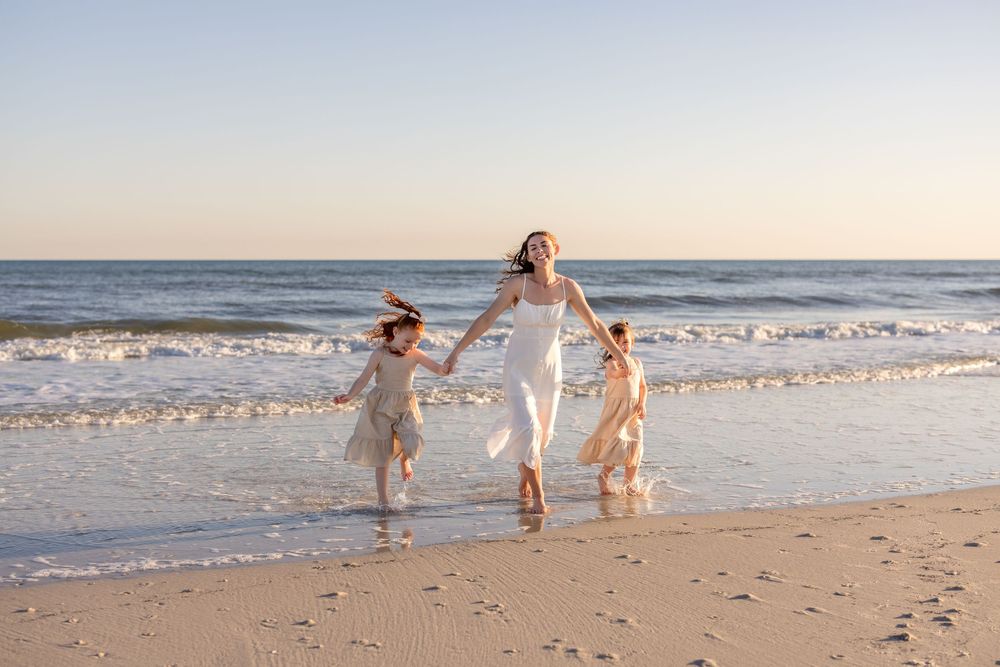 A family plays together on a sandy beach at sunset with gentle waves rolling in the background.