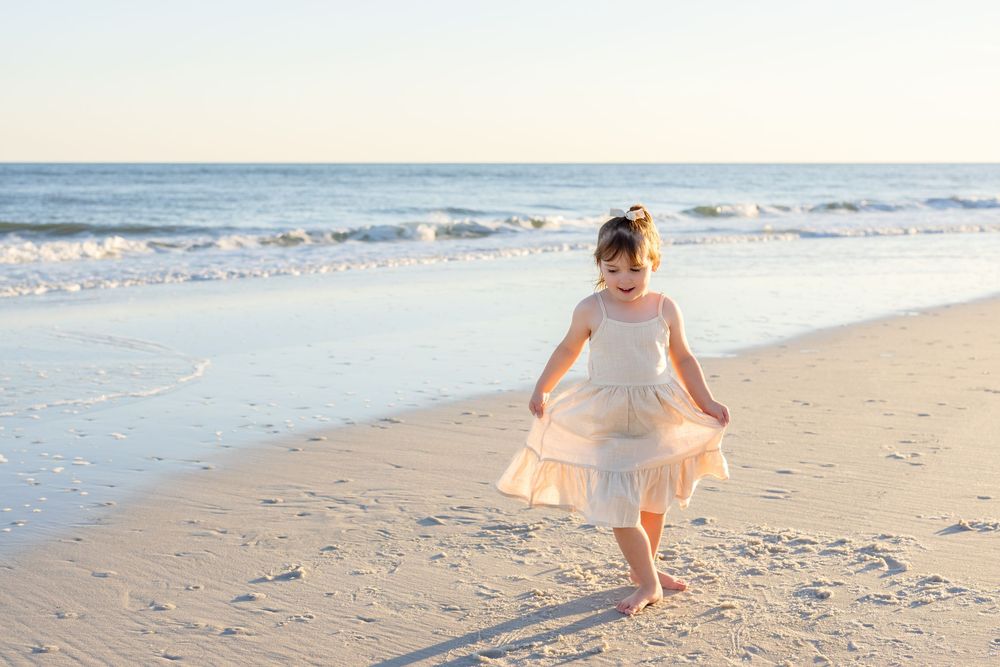 A figure in a flowing dress twirls joyfully on the beach with waves rolling in the background.