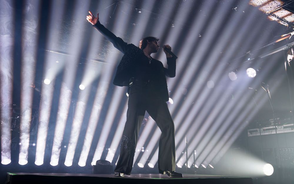 Performer on stage with dramatic backlighting and bright stage lights during a live concert performance.