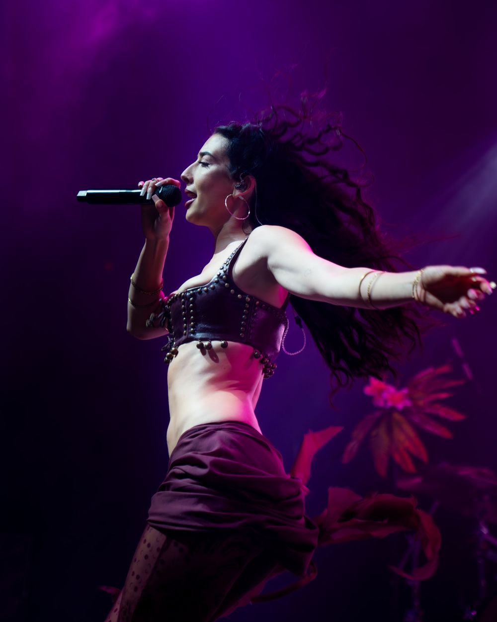 Female singer performing on stage with microphone, dramatic lighting, flowing dreadlocks, wearing black crop top.