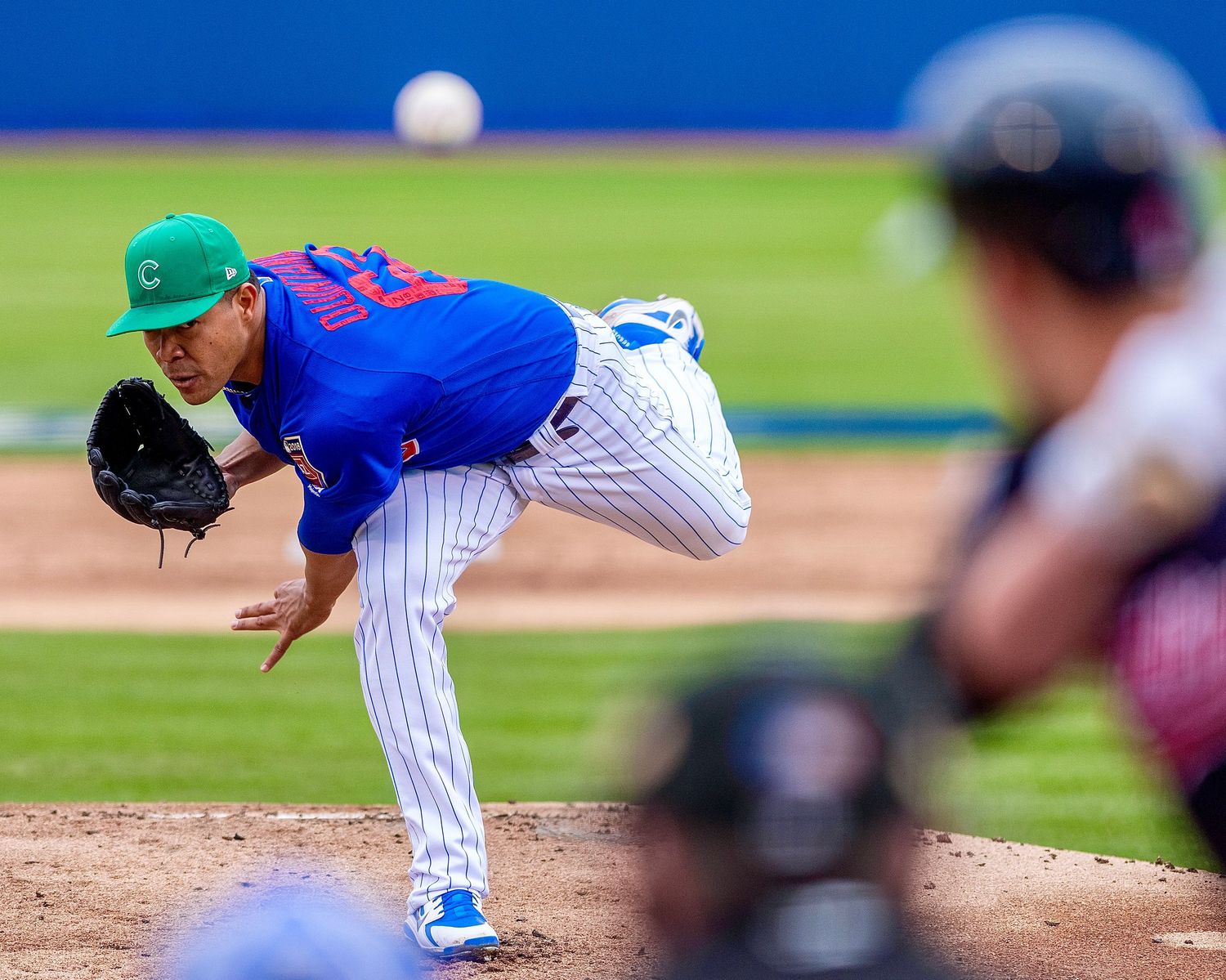 Baseball pitcher in blue uniform and green cap follows through on delivery during game.