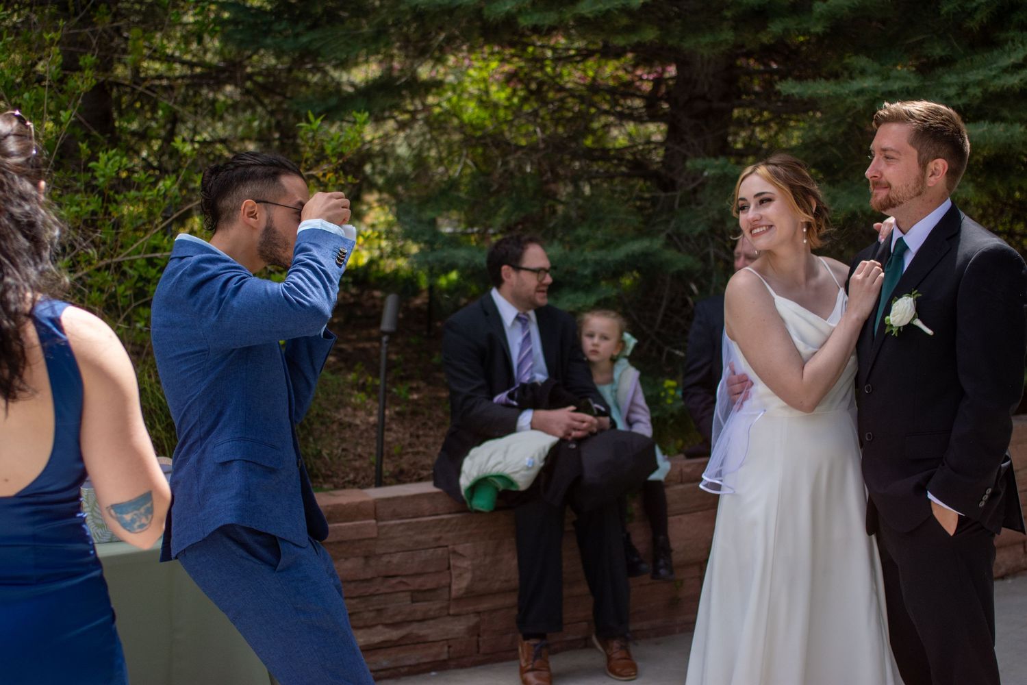 Wedding party celebrates outdoors with champagne toasts in a garden setting.