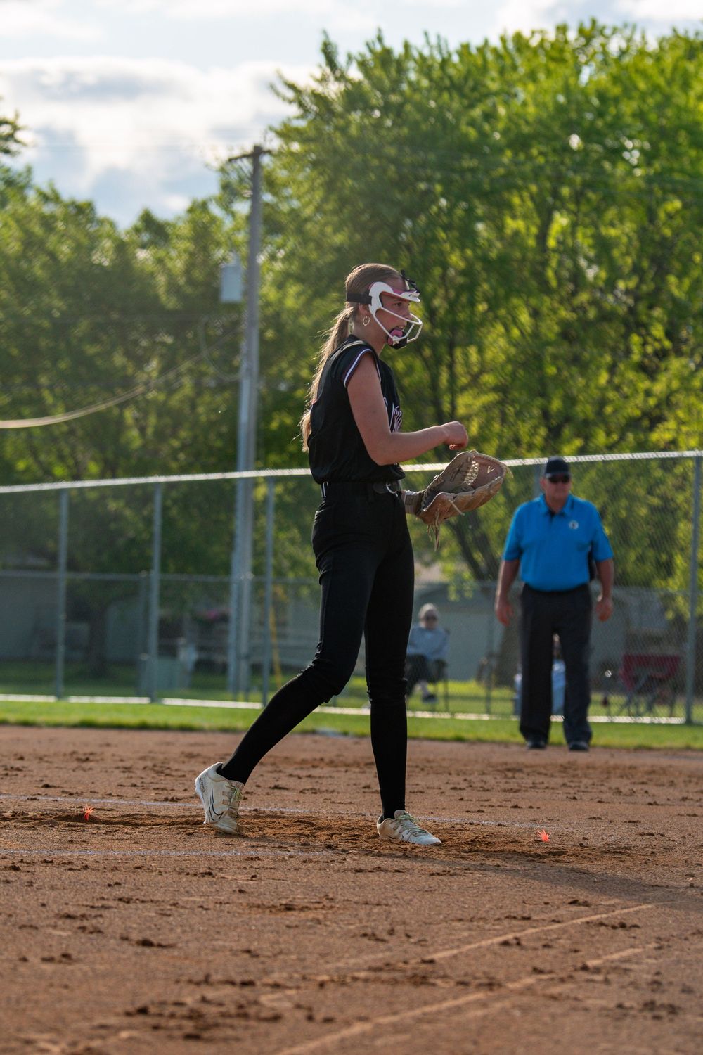 Softball pitcher in dark uniform winds up for pitch delivery on dirt field.