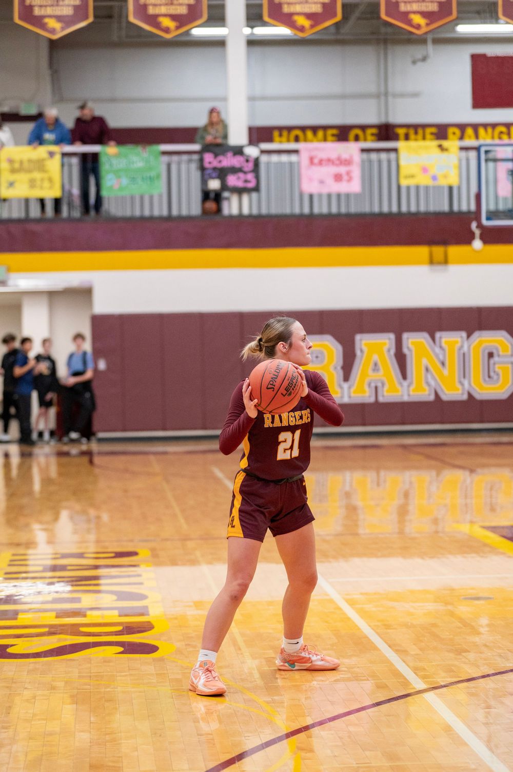 Volleyball player in maroon uniform dives for the ball on a polished gymnasium floor during a match.