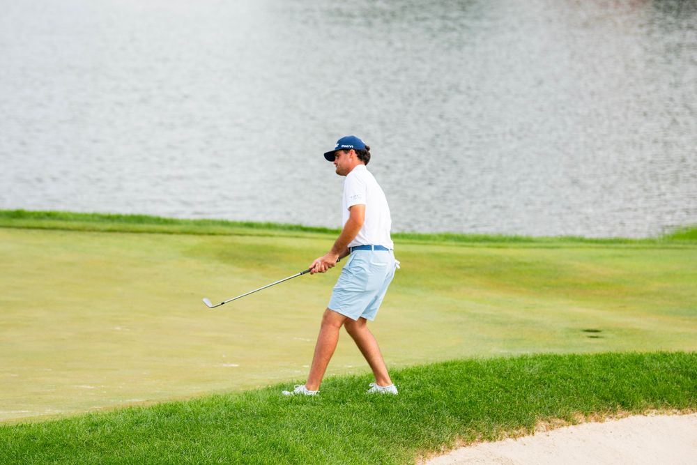 Golfers practice putting on a lush green course near a water hazard.