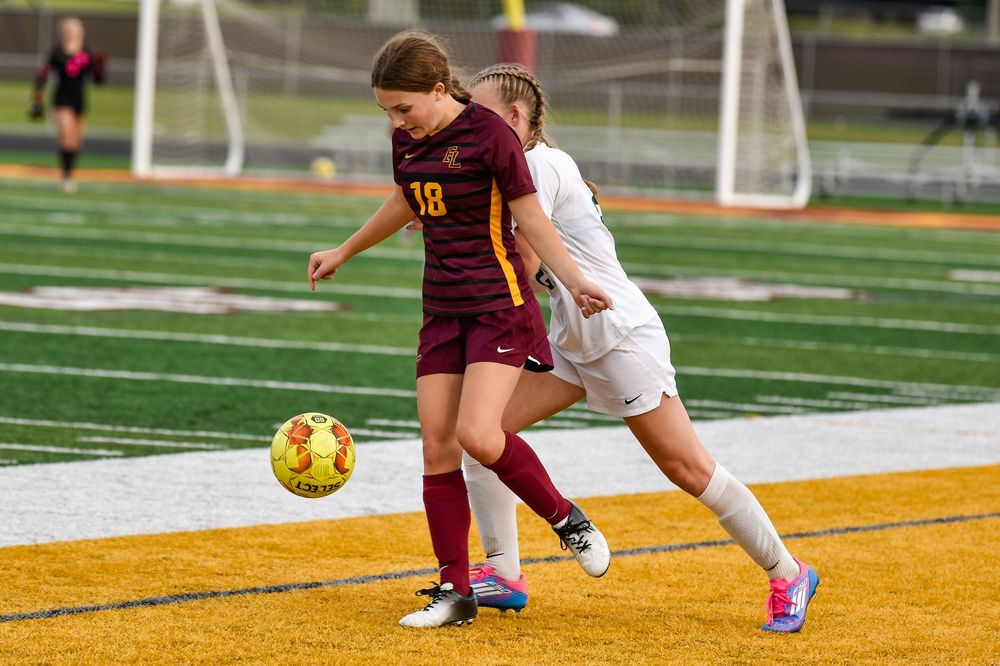 Soccer players compete for ball control during match on turf field.