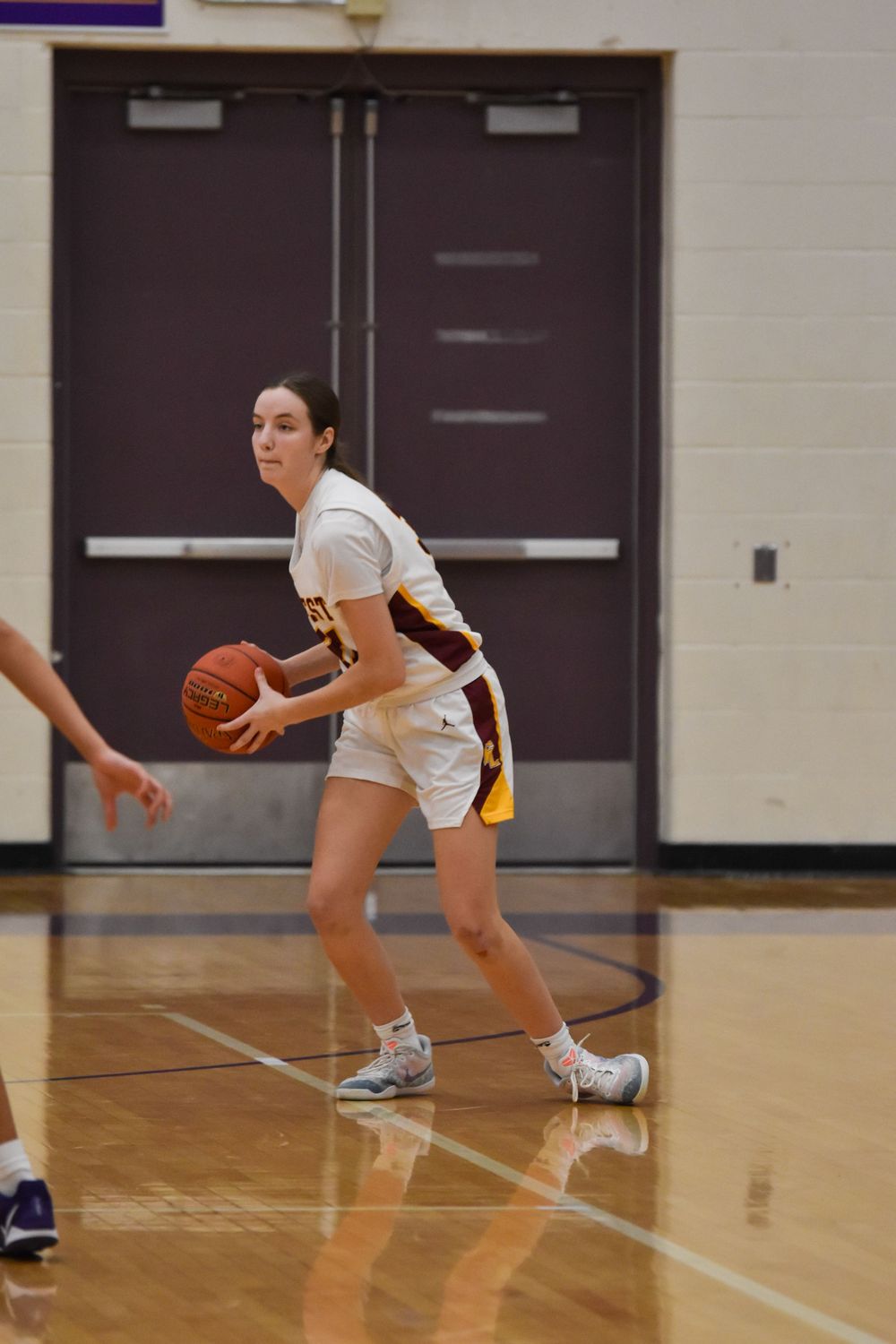 Basketball player in white uniform scans court while controlling ball during game.
