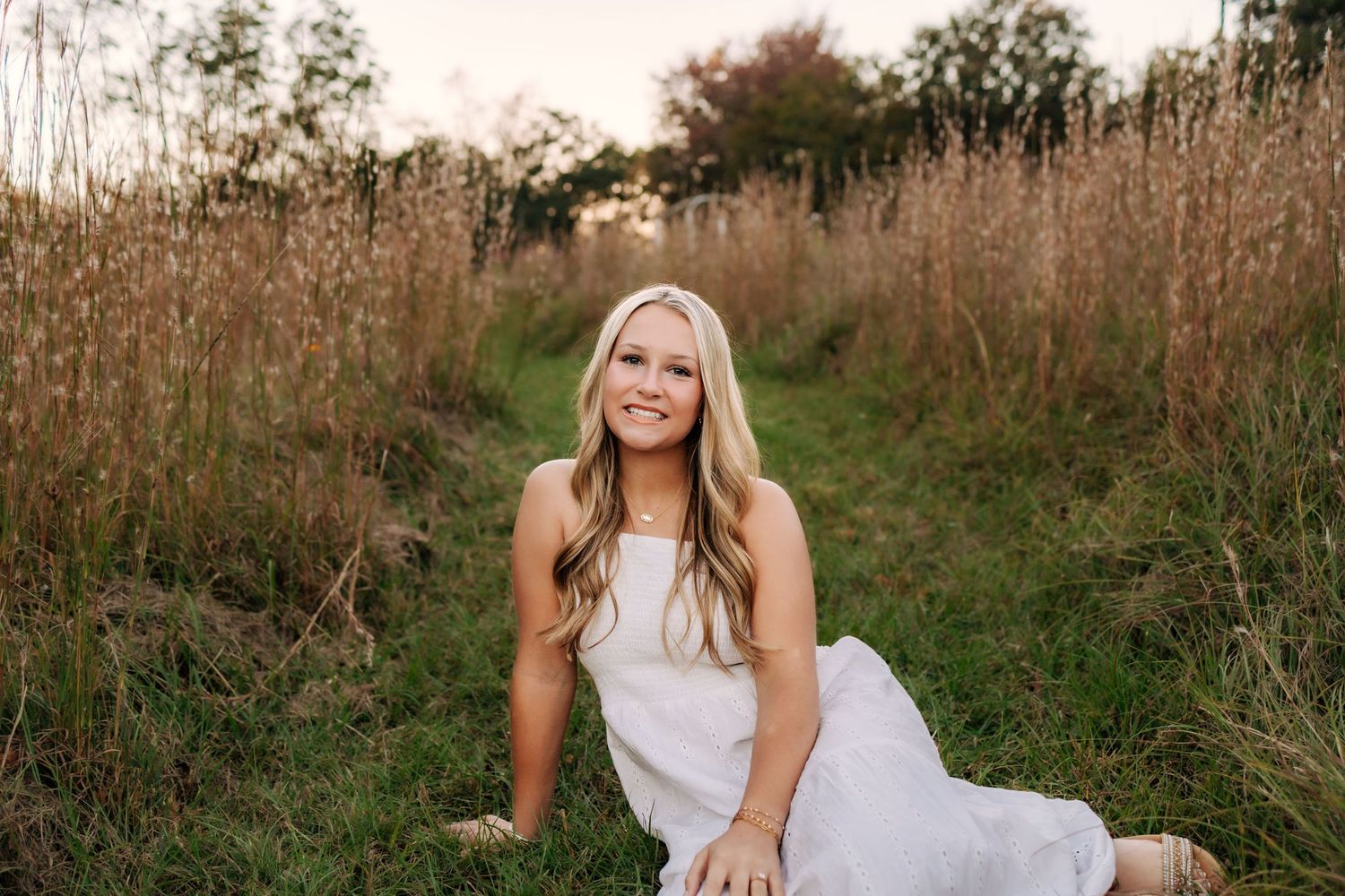 Woman in white dress poses gracefully in golden field during sunset photoshoot.