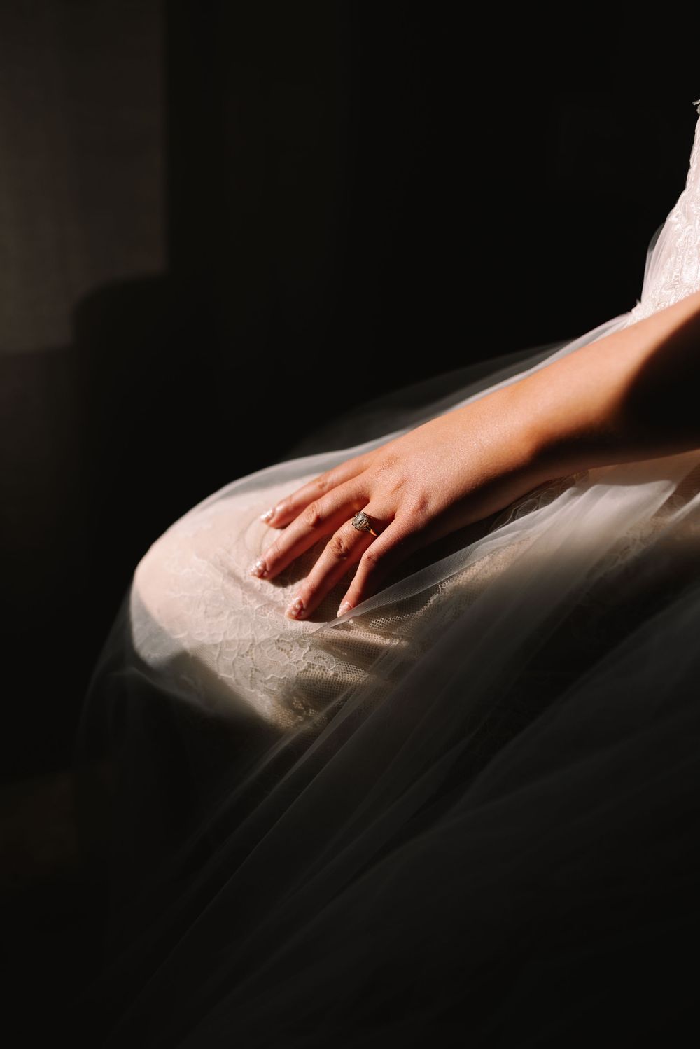 Close-up of a bride's hand with a ring resting on her white tulle wedding dress.
