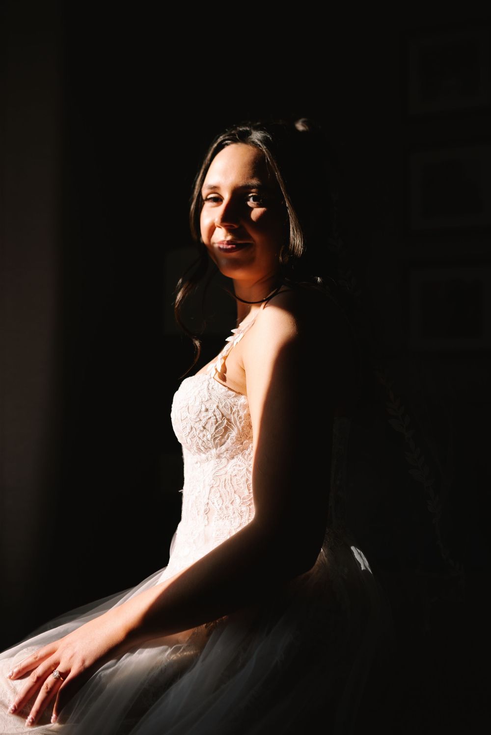 Beautiful bride in a white lace wedding dress posing in dramatic light and shadow.