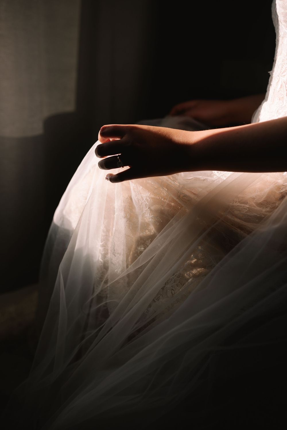 Close-up of a bride's hands holding the flowing tulle skirt of her wedding gown in dramatic light.