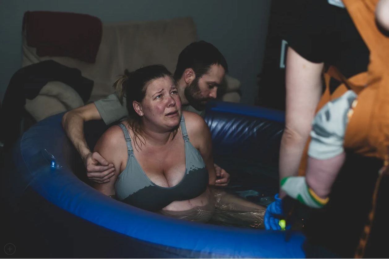 A labor support scene in a blue birthing pool during a home birth.