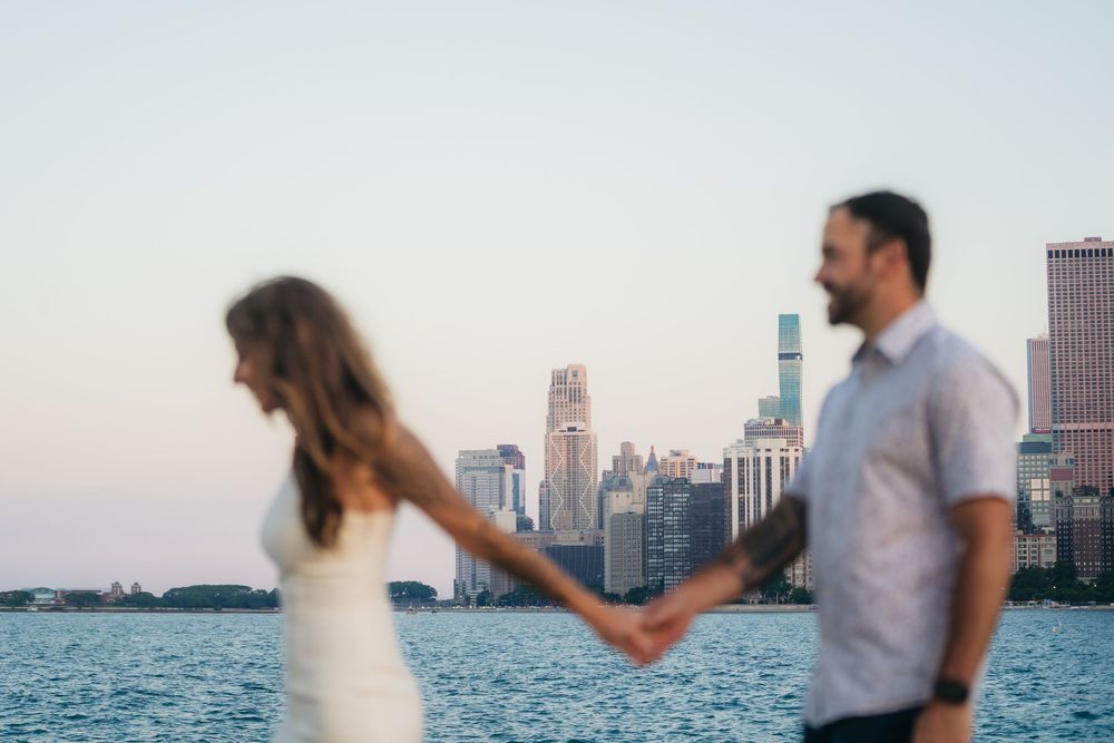 Couple holding hands during engagement session with Chicago skyline and lake Michigan in background at sunset.