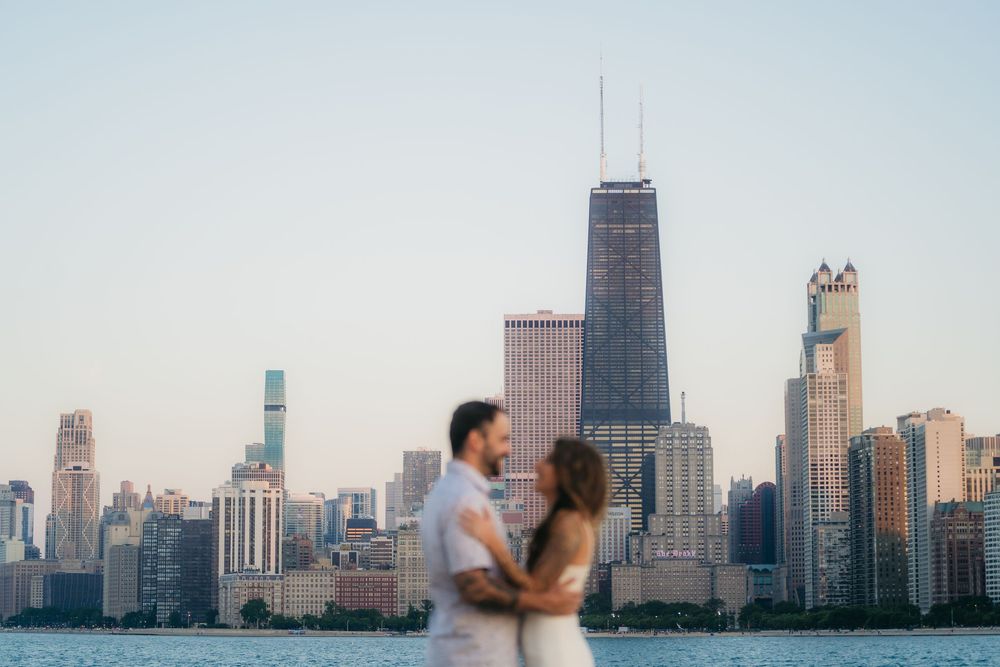 Couple embracing with Chicago skyline and John Hancock Center in background during golden hour engagement photo.
