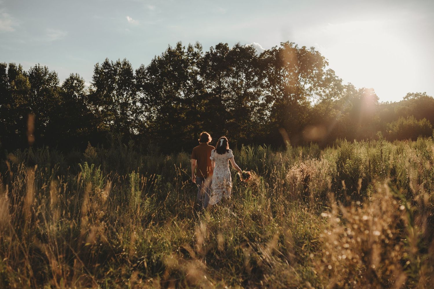 A young couple sits together in a golden field at sunset, the woman leaning on the man's shoulder.