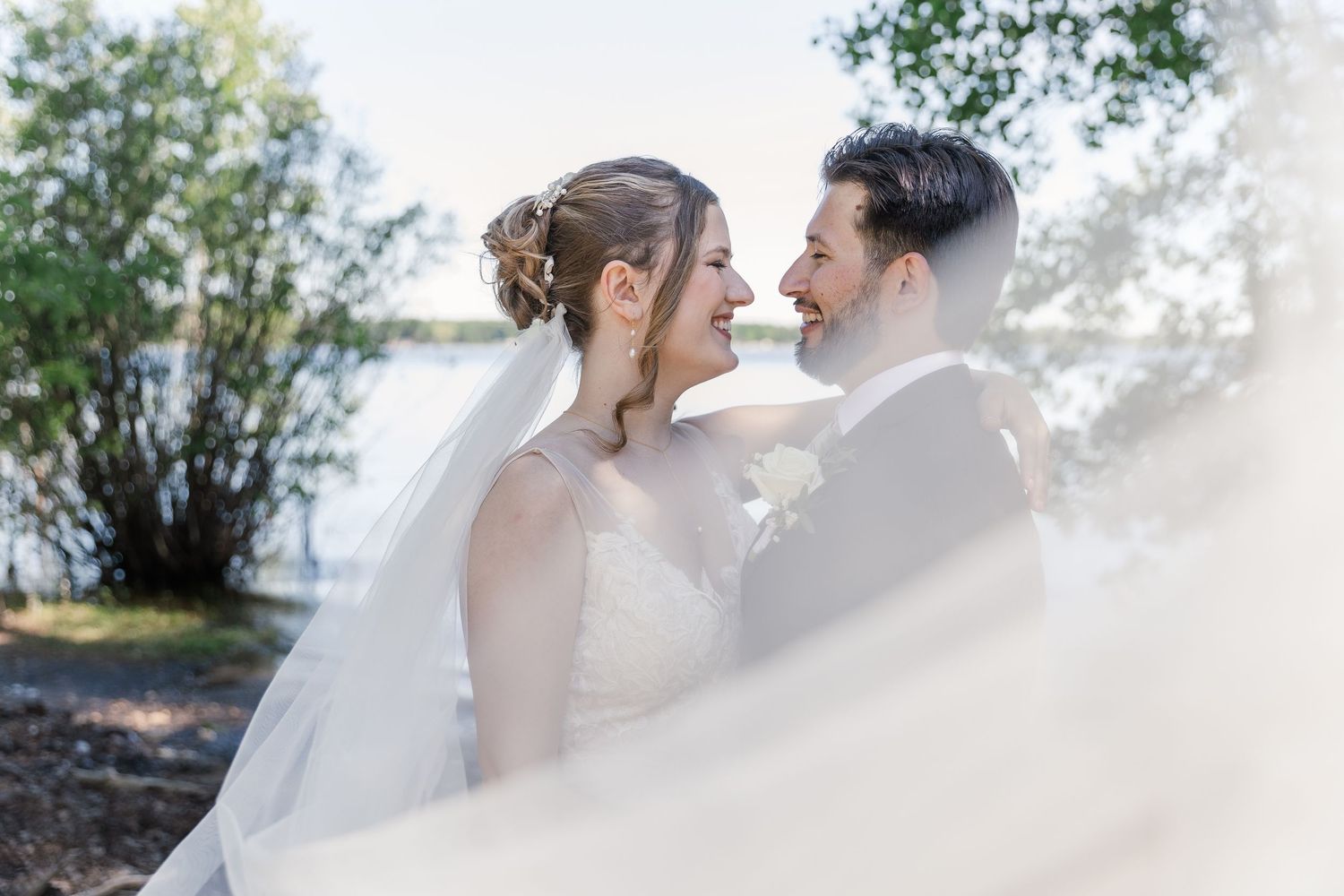 Bride and groom stand together in front of the lake during their summer wedding photos near woodstock, ontario.