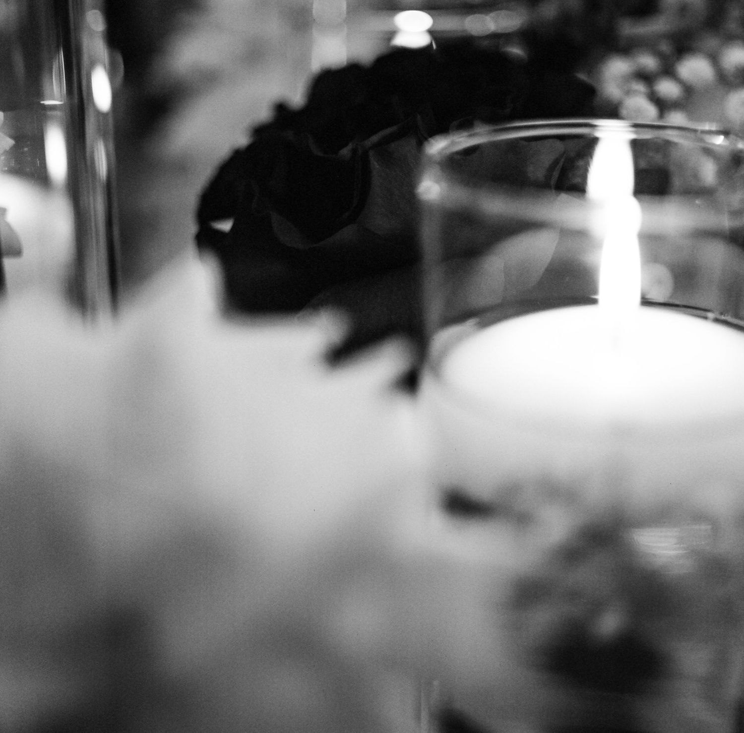 Black and white photo of a glowing candle in a glass holder with soft floral bokeh background.