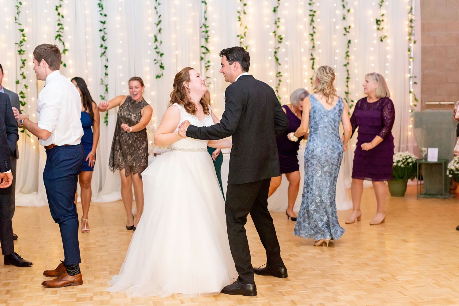 Bride and groom share first dance at elegant wedding reception with guests dancing in background.