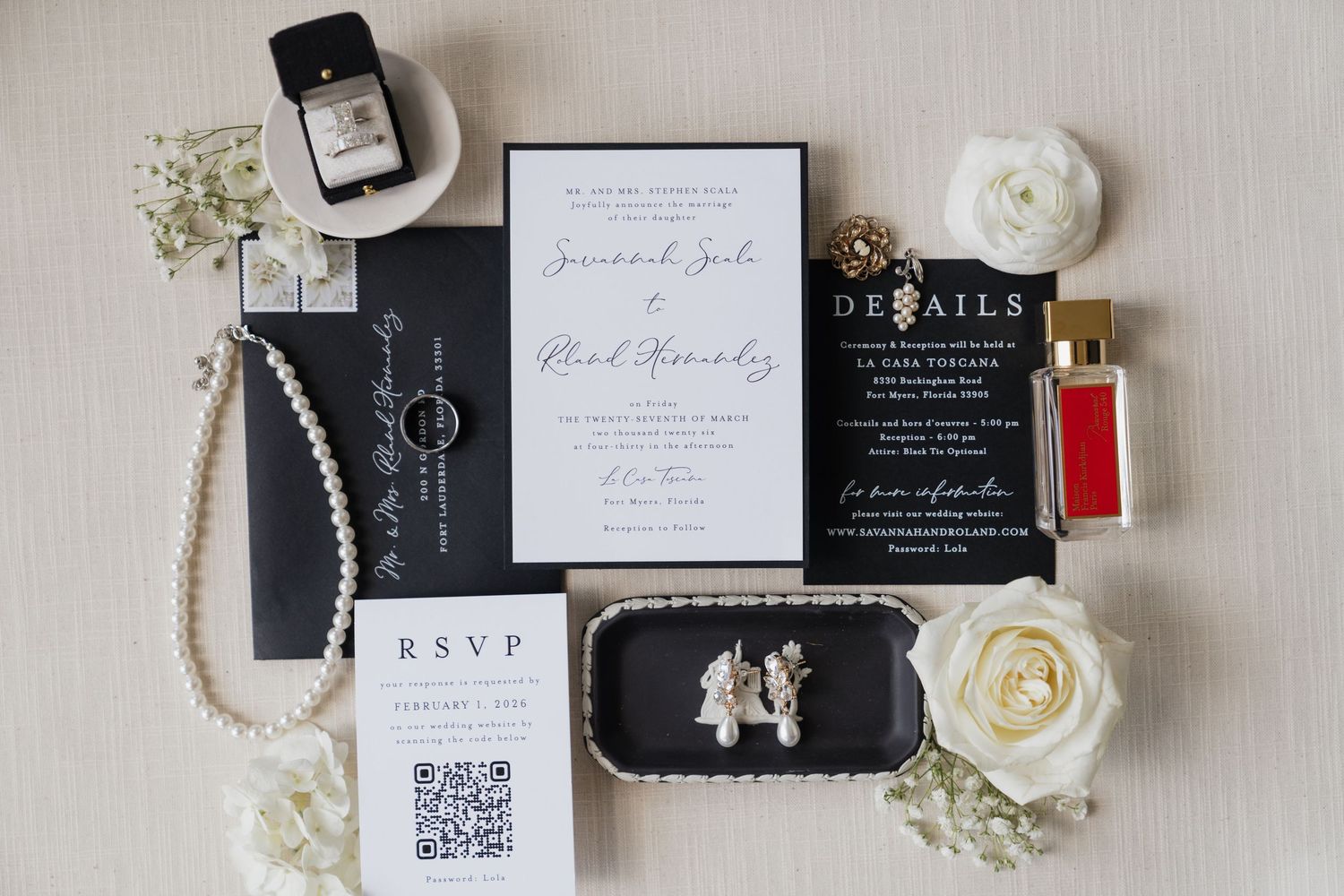 Elegant black and white wedding invitation suite with pearl necklace, roses, perfume, and gold jewelry accents on white background.