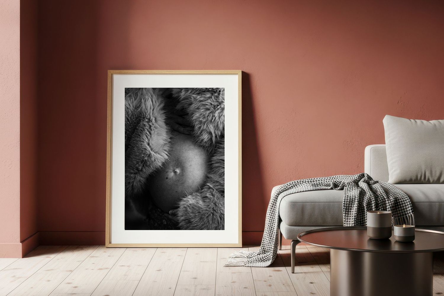 Black and white maternity photo print in gold frame displayed in modern living room with rose-colored walls.