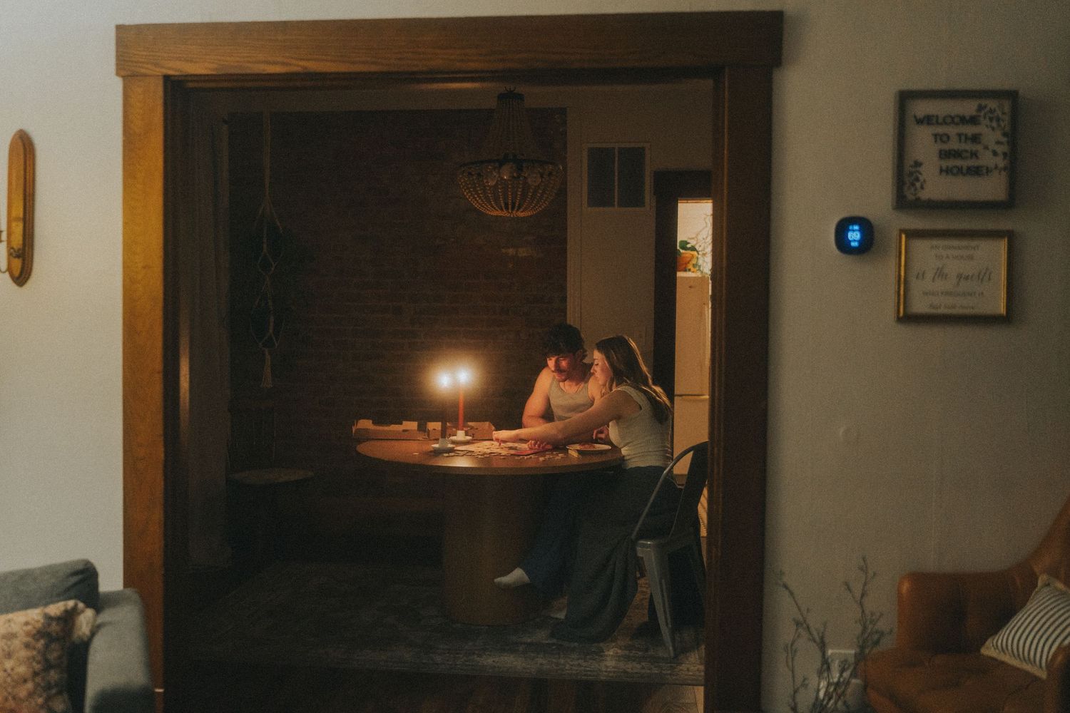 Couple sharing a romantic candlelit dinner at a round table in a dimly lit dining room at night.