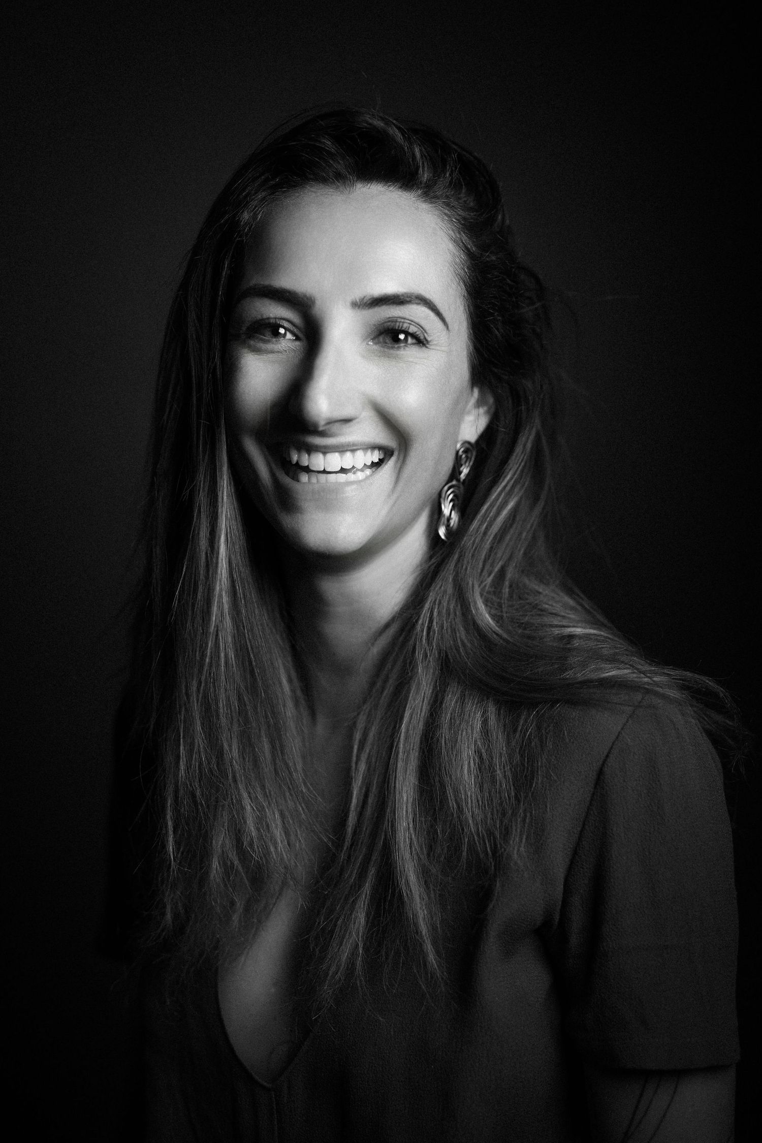 Black and white portrait of a smiling young woman with long hair wearing earrings and a dark top.