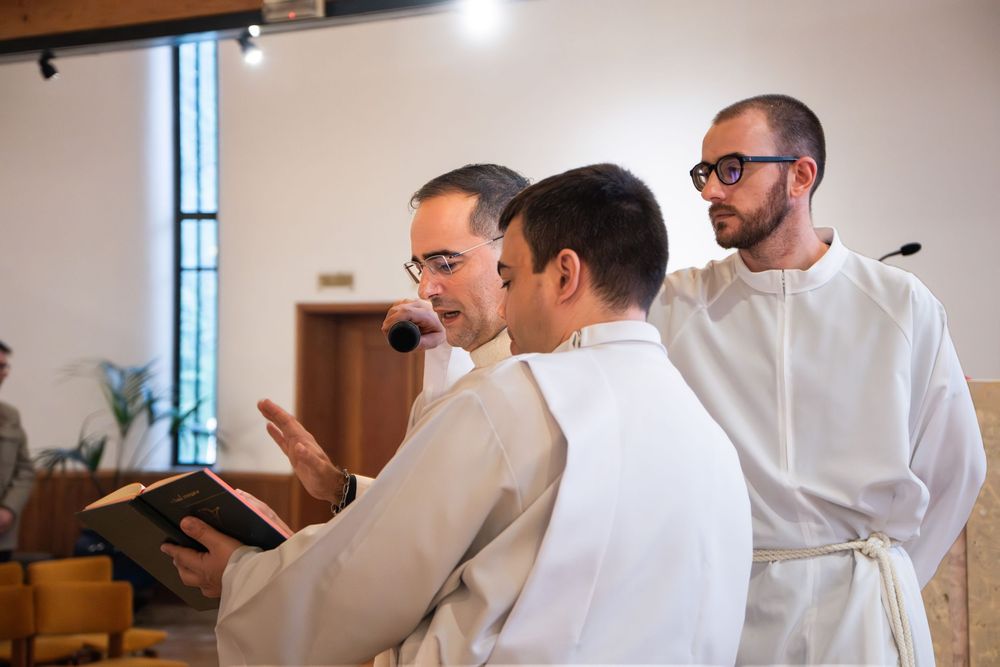 Three clergy members in white robes reading from a book during a religious ceremony in a church.