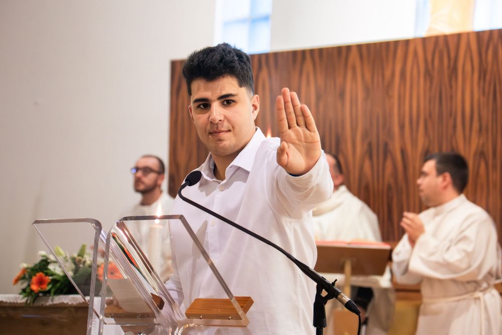 Young man in white shirt raises hand at church podium during religious ceremony.