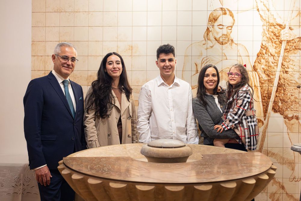 Five people smiling together in an elegant room with a decorative wooden table and ornate mosaic wall art.