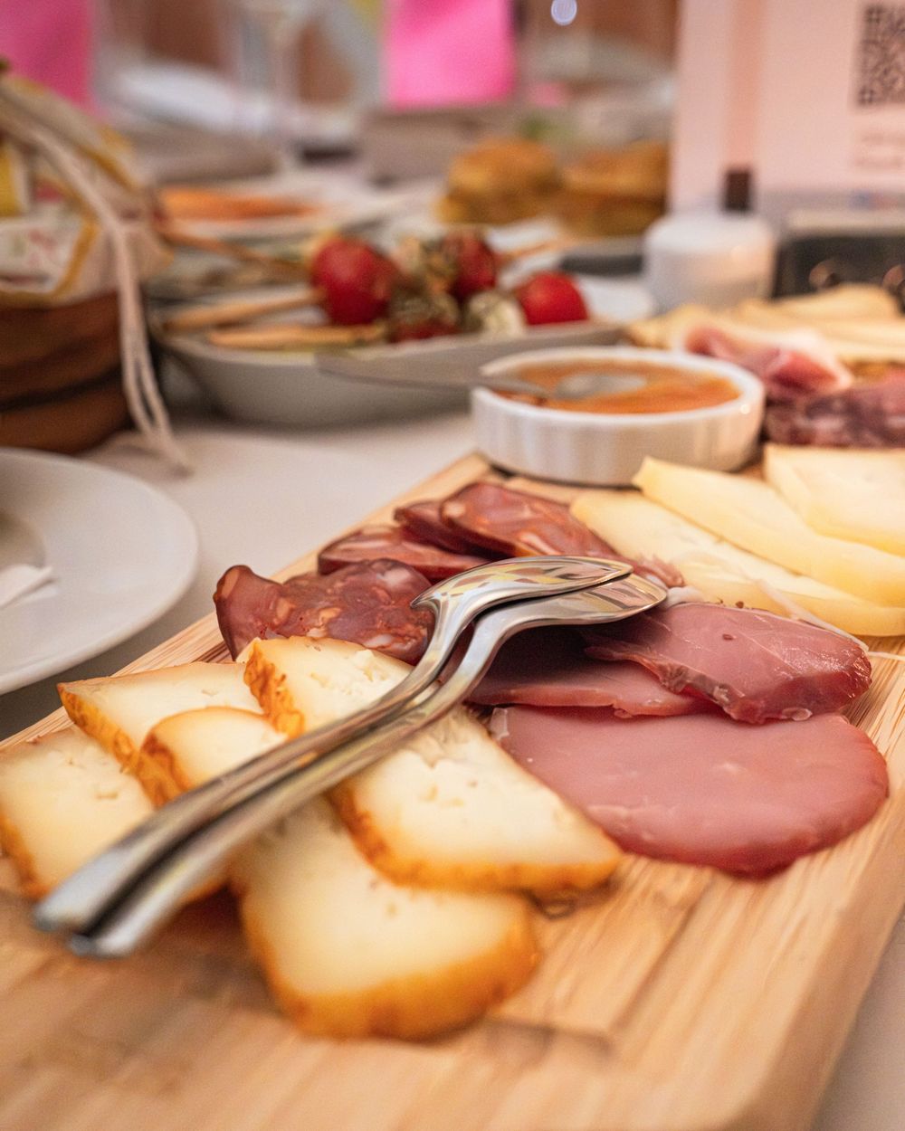 Charcuterie board with sliced meats, cheese, and toast on wood, with strawberries and dipping sauce in background.